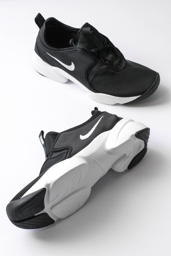 From above of sports shoes pair with black breathable surface and white soles comfortable suiting on feet placed on white background