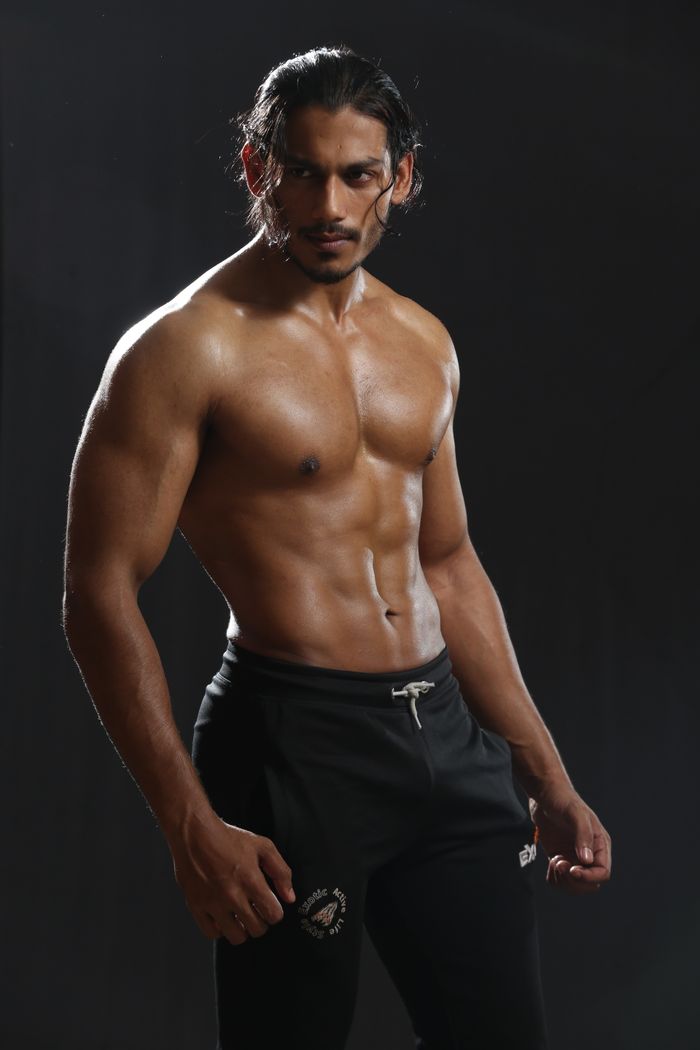 Powerful studio image of a muscular male model posing in sportswear against a dark background.