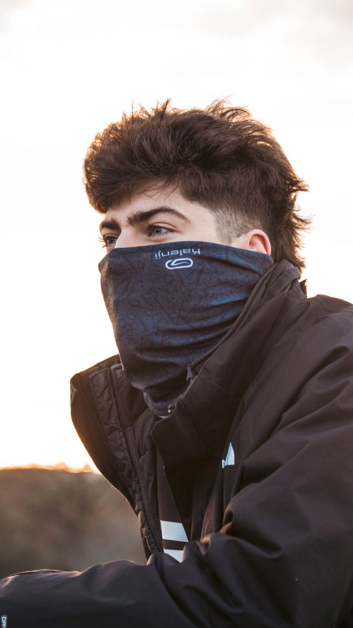 Portrait of a young man wearing a scarf and jacket outdoors at sunset.
